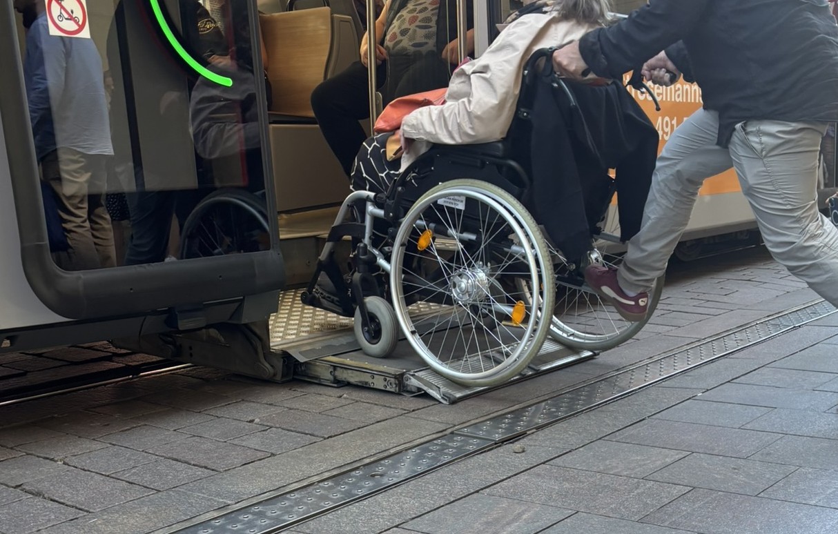 Die Rollstuhlrampe einer Straßenbahn fährt aus, dass eine Person im Rollstuhl in die Bahn kommt